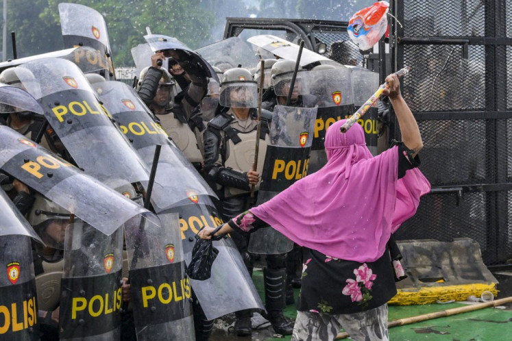 A woman strikes a police officer with a bamboo stick as police push back students during a protest outside the House of Representatives building against lawmakers demands for higher allowances in Jakarta on August 28, 2025.