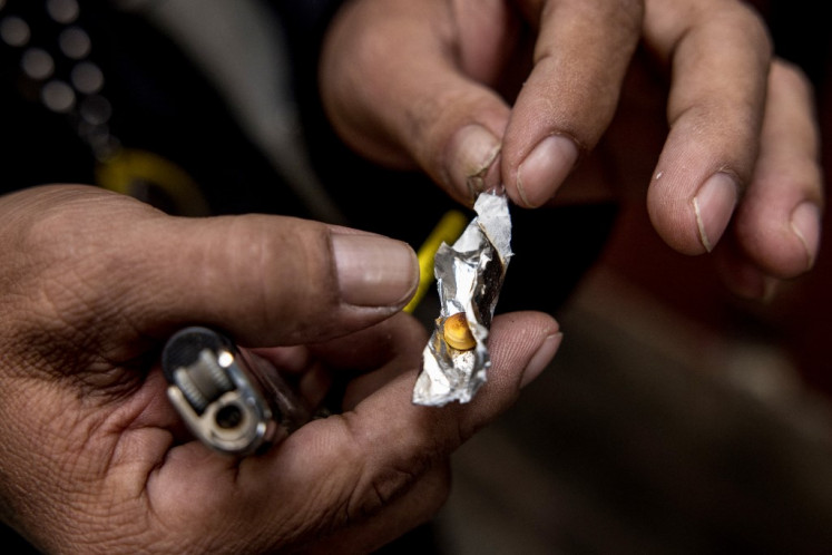 Motorbike taxi driver Soonthorn poses for photos as he holds a yaba methamphetamine pill while demonstrating how he consumes the drug during an interview with AFP in Bangkok on Jan. 12, 2021.