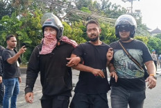 Two plainclothes police personnel detain a demonstrator in front of the Bali Police headquarters in Denpasar on Aug. 30, 2025. 