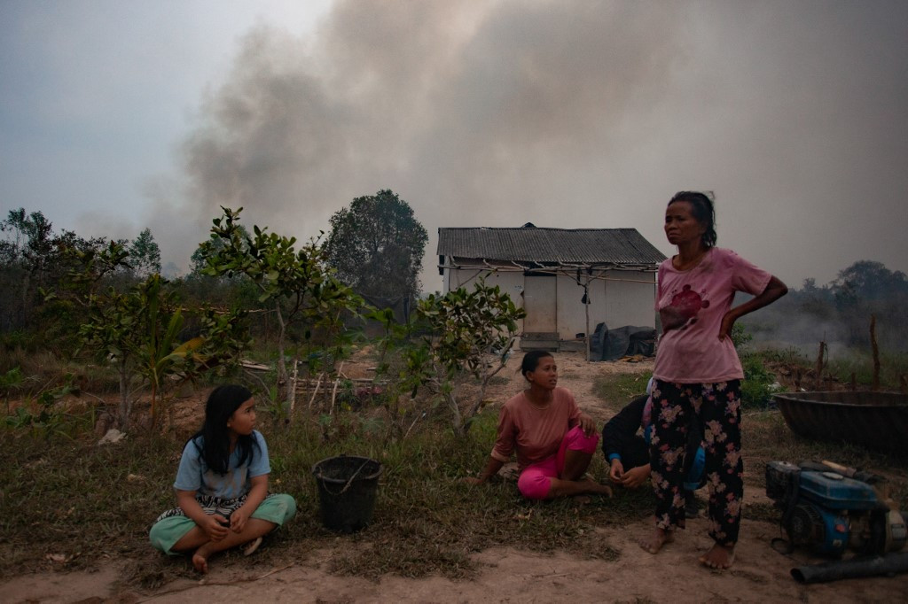 Agustini, 30 (center) sits in front of her hut as a forest fire approaches in Ogan Ilir regency, South Sumatra on Oct. 10, 2023.