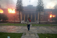 A man with the Nepalese flag draped around his neck walks away from Rastrapati Bhawan, the presidential residence and office in Kathmandu, as flames burn through the structure on Sept. 9, 2025.