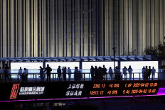 An electronic board shows Shanghai and Shenzhen stock indices as people walk on a pedestrian bridge at the Lujiazui financial district in Shanghai, China, on April 2, 2025.
