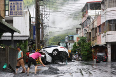 Residents clear mud from their property, while damaged cars are seen in the background, in Hualien on September 24, 2025, following the bursting of a barrier lake. At least 14 people were killed when a decades-old lake barrier burst in Taiwan, a government official said on September 24, after Super Typhoon Ragasa pounded the island with torrential rains.