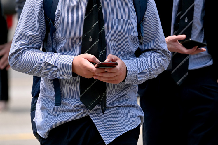 A file photo taken on November 28, 2024 shows people looking at their phones in Melbourne, Australia. 