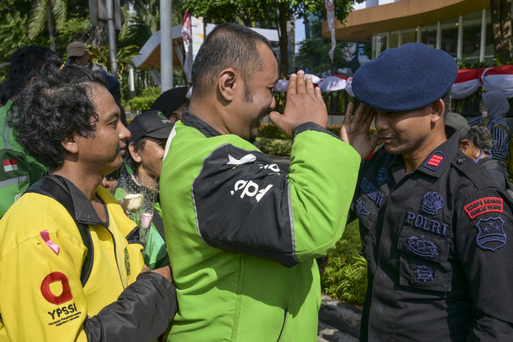 An ojol (online motorcycle transportation) driver (center) and police officer (right) salute each other during a peace rally in Jakarta on Sept. 2, 2025, after deadly protests following the killing of a young ojol driver by police tactical vehicle. At least 10 people died during violent protests sparked by lavish perks for lawmakers that have widened to include anger against police brutality.