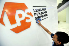An employee cleans the signage of the Deposit Insurance Corporation (LPS) at its office building in Jakarta in 2018. 