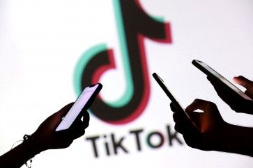 Teenagers pose for a photo while holding smartphones in front of a TikTok logo in this illustration taken September 11, 2025.