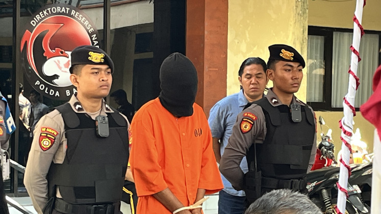 A Dutch man, 31, identified only as NR, stands with his head covered by a black ski mask and his hands restrained with zip ties, guarded by police during a press conference on Oct. 3 at the Bali Police Headquarters in Denpasar. NR was arrested on Oct. 1 after police allegedly discovered a hydroponic cannabis farm inside his rented house. He is currently facing charges that carry the death penalty.