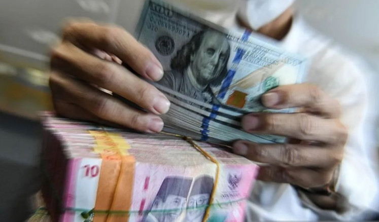 A teller holds a quantity of 100 United States dollar bills atop a bundle of 100,000 Indonesian rupiah banknotes on May 15, 2025, at a money changer in Jakarta.