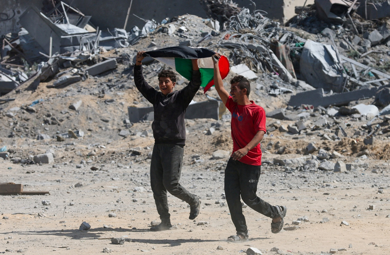 A pair of Gazanz the Palestinian flag near rubble in Khan Younis in the southern Gaza Strip on Oct. 10, 2025, following Israeli forces' withdrawal from the area after Israel and Hamas agreed on the Gaza ceasefire.