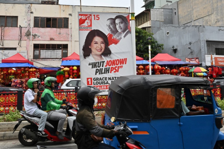 Jakarta motorists drive on Jan. 18, 2024, past a campaign banner for legislative candidate Grace Natalie Louisa from the Indonesian Solidarity Party (PSI) that also features party chair Kaesang Pangarep (right, top) and his father, then-president Joko “Jokowi” Widodo. (AFP/Adek Berry)