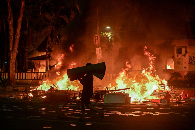 Two wrongs: A person carries looted goods past a burning police station targeted by violent protests on Aug.31, 2025 in Surabaya, East Java.

