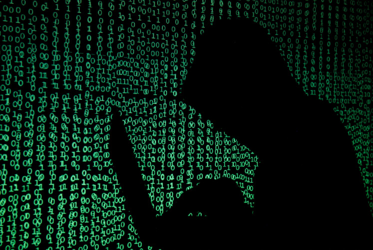 A hooded man with a laptop computer is silhouetted against a projection of binary code, in this illustration created on May 13, 2017.