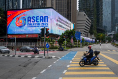 A man rides his motorcycle past a big screen showing the logo of the Association of Southeast Asian Nations (ASEAN) in front of Malaysia's Petronas Twin Towers ahead of the 47th ASEAN Summit in Kuala Lumpur on October 23, 2025.