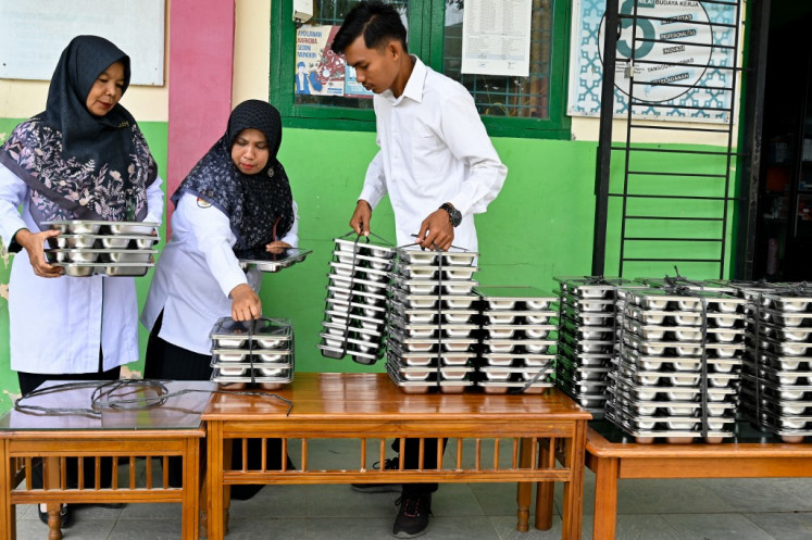 Teachers collect trays of food for their students supplied by President Prabowo Subianto's flagship free nutritious meal program on Oct. 13  at an elementary school in Darul Kamal, Aceh.