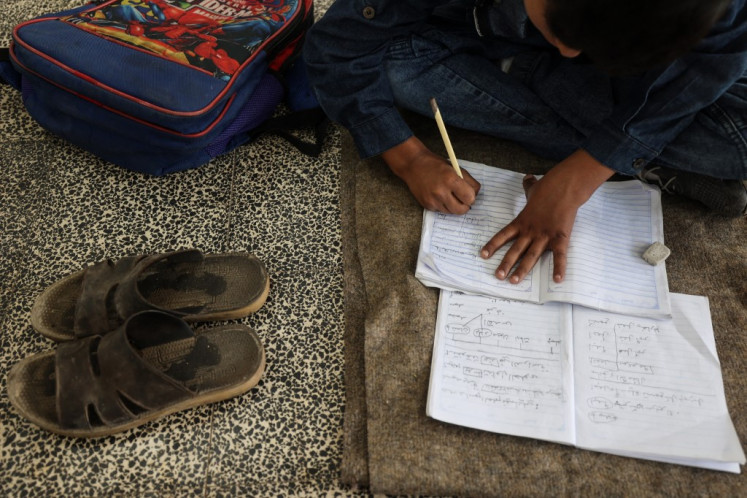A Palestinian boy takes notes on his notebook at a school in the Nuseirat refugee camp, in the central Gaza Strip, on Oct. 26, 2025, after a United States-brokered ceasefire came into effect earlier in the month. With Gaza's education system shattered by two years of gruelling war, UNICEF's regional director said on Oct. 23 that he feared for a “lost generation“ of children wandering ruined streets with nothing to do.