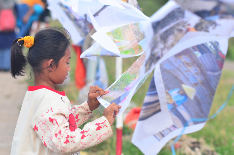 Self-reflection: Fina, 9, a participant of Kelas Jurnalis Cilik (young journalists class), looks at her fabric-printed photograph on Nov. 1, 2025, during the opening ceremony of INFINITI: Imajinasi dan Fantasi Sejak Dini (Infinity: Imagination and fantasy from an early age), a photo exhibition that ran from Oct. 31 to Nov. 2 in Cilincing, North Jakarta. (JP/Iqro Rinaldi)