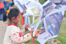 Self-reflection: Fina, 9, a participant of Kelas Jurnalis Cilik (young journalists class), looks at her fabric-printed photograph on Nov. 1, 2025, during the opening ceremony of INFINITI: Imajinasi dan Fantasi Sejak Dini (Infinity: Imagination and fantasy from an early age), a photo exhibition that ran from Oct. 31 to Nov. 2 in Cilincing, North Jakarta. (JP/Iqro Rinaldi)