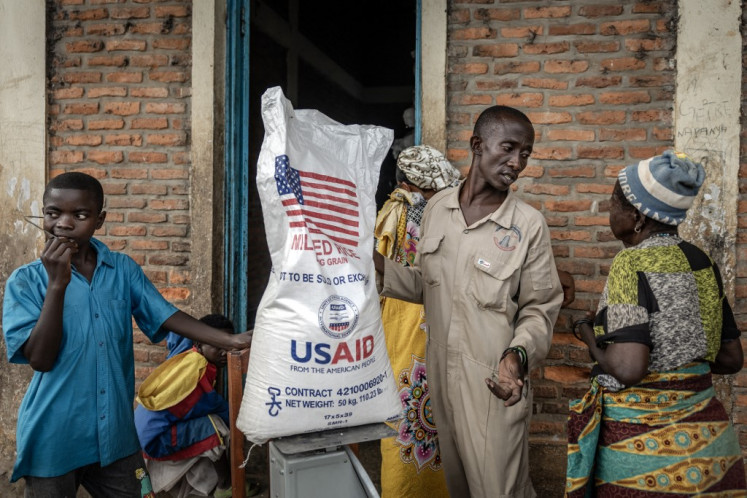 A Burundian government official from the Office for the Protection of Refugees speaks with newly arrived Congolese refugees awaiting relocation while weighing a sack of rice from the final batches delivered by the now-dismantled United States Agency for International Development (USAID) following a food distribution at the Cishemere Transit Center near Buganda, on May 6, 2025. 