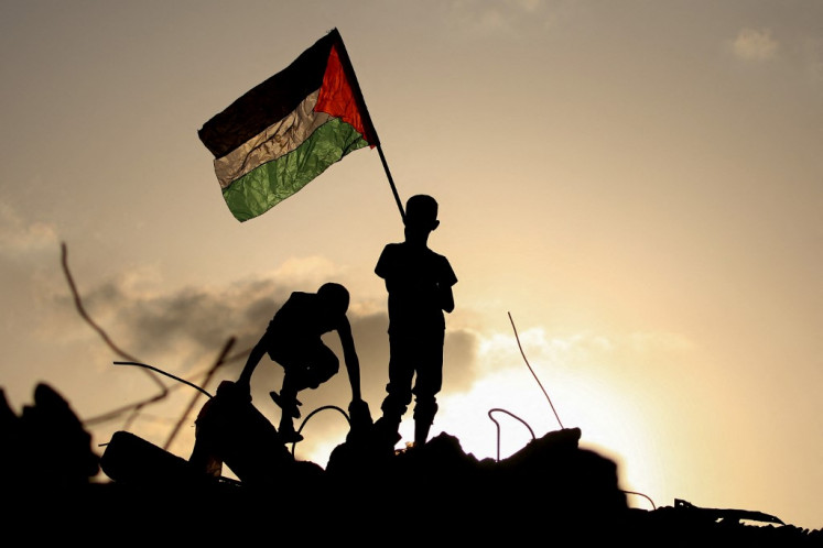Displaced Palestinian children wave the Palestinian national flag as he stands on the rubble of a destroyed building at the Bureij camp for refugees in the central Gaza Strip on Sept. 22, 2025.