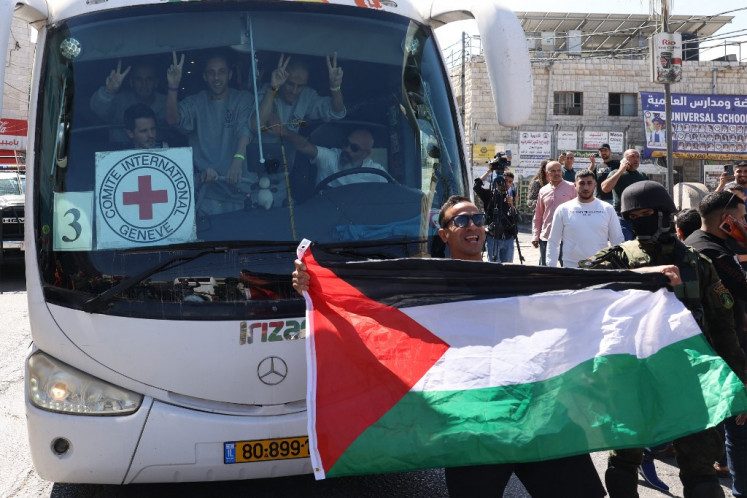 A man holds up a Palestinian national flag in front of a bus carrying former prisoners released by Israeli forces from the Ofer military prison located between Ramallah and Beitunia in the occupied West Bank on Oct. 13, 2025, in exchange for hostages held by Hamas in Gaza since the Oct. 7, 2023, attacks. 