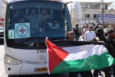 A man holds up a Palestinian national flag in front of a bus carrying former prisoners released by Israeli forces from the Ofer military prison located between Ramallah and Beitunia in the occupied West Bank on Oct. 13, 2025, in exchange for hostages held by Hamas in Gaza since the Oct. 7, 2023, attacks. 