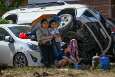 People rest beside cars, swept one on top of another by floodwaters caused by typhoon Kalmaegi, in Liloan in the province of Cebu on November 6, 2025. Typhoon Kalmaegi killed at least 140 people and left another 127 missing after unleashing devastating flooding across the central Philippines, official figures showed, as the storm headed towards Vietnam. (Photo by Jam STA ROSA / AFP)