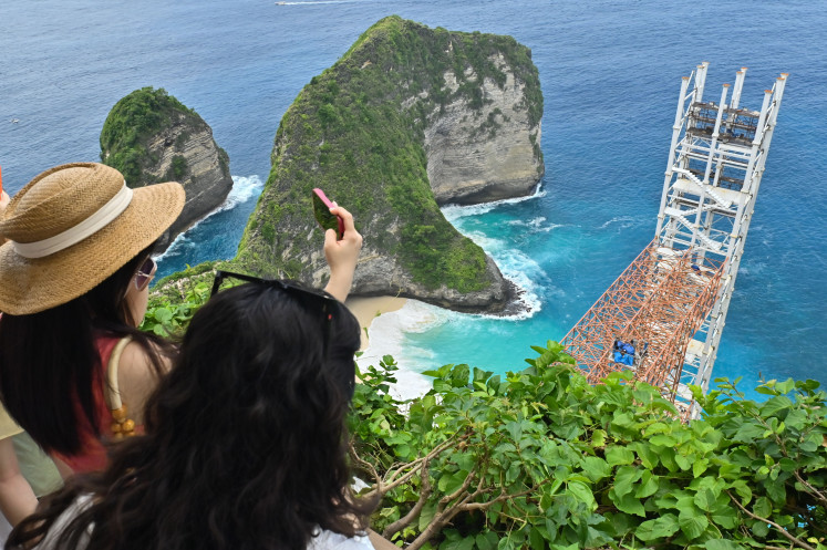 Tourists take photos on Nov. 5, of the beach with a glass elevator obstructing the view at Kelingking Beach on Nusa Penida Island in Klungkung regency, Bali. Bali Governor Wayan Koster has ordered the project's investor to stop and dismantle the construction and return the beach to its original state.