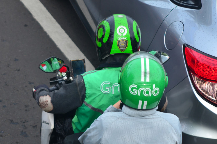 Logos of “Go-Jek” and “Grab” are seen on the helmets of an online motorcycle taxi driver and his passenger on Nov. 12 in a traffic jam on Jl. Basuki Rachmat in Jakarta.