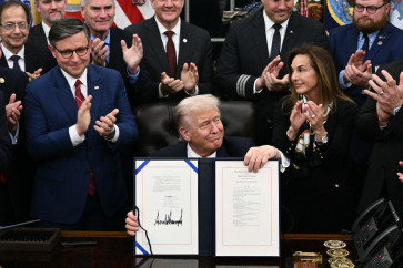US President Donald Trump shows the signed bill package to re-open the federal government as the Speaker of the House Mike Johnson (left) and other Republican leaders applaud in the Oval Office of the White House in Washington, DC, on Nov. 12, 2025.