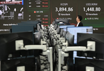 A currency dealer walks past a screen showing South Korea's benchmark stock index and the Korean won/USD exchange rate in a foreign exchange dealing room at the Hana Bank headquarters in Seoul on Nov. 5, 2025.