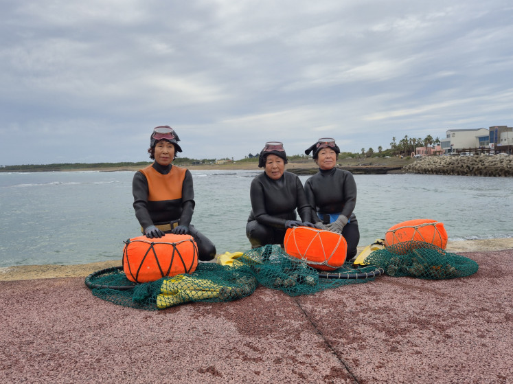 'Haenyeo', skilled female free divers, from Sagye-ri village in Jeju, South Korea, (from left) Lee Han-ok, 68, Kim Su-seon, 74, and Lee Bok-soo, 71, pose for a photo with the seafood they have brought back from their dives on Nov. 12, 2025.