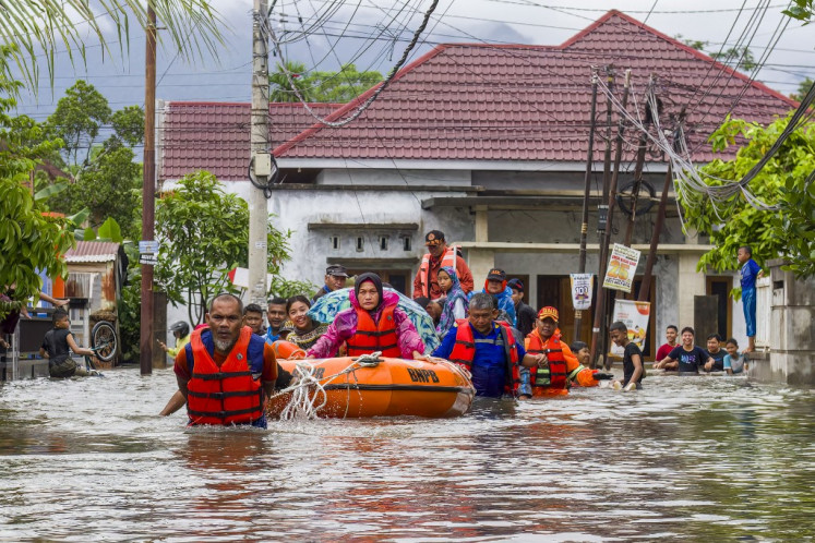 A rescue team evacuates women and children in a rubber boat as floodwaters hit a residential area in Padang, West Sumatra on November 25, 2025.