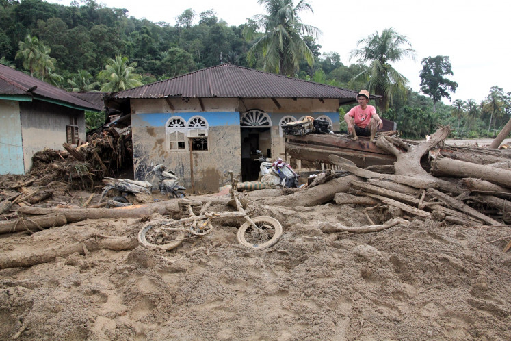 A man sits on debris on Friday after it was carried by floodwater and struck a house in South Tapanuli regency, North Sumatra. Extreme weather has triggered floods and landslides in the region since Nov. 25. 
