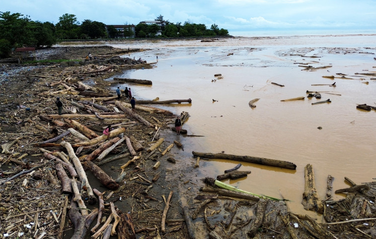 Residents walk among piles of large timber washed ashore on Air Tawar Beach in Padang, West Sumatra, on Friday, Nov. 28, 2025. The logs accumulated along Padang’s coastline following recent flash floods. 