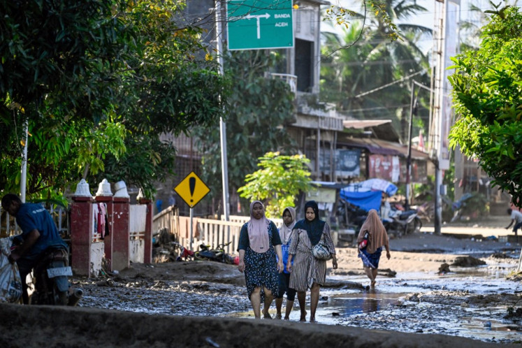 People walk on a mud-covered road following flash floods in Meureudu, Pidie Jaya district in Aceh province on November 29, 2025. 