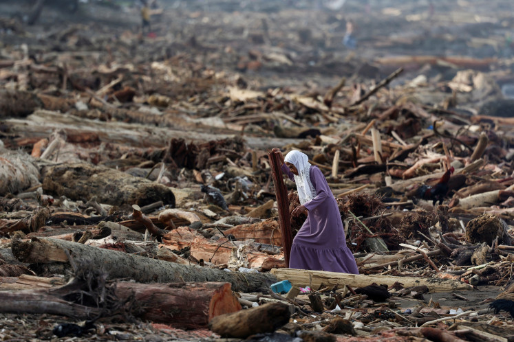 A woman walks among tree trunks on the shore on Sunday following deadly flash floods and landslides, in Padang, West Sumatra. The death toll from floods that hit Indonesia this week has reportedly risen to more than 400 people.