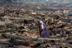 A woman walks among tree trunks on the shore on Sunday following deadly flash floods and landslides, in Padang, West Sumatra. The death toll from floods that hit Indonesia this week has reportedly risen to more than 400 people.