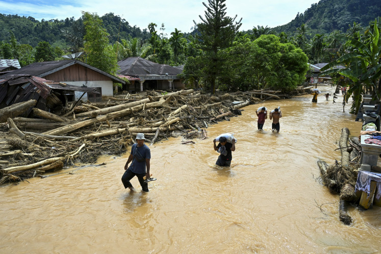 People wade through the floodwater in the aftermath of flash floods at Tukka village, Central Tapanuli, North Sumatra, on December 2, 2025. The death toll from floods and landslides that have struck Indonesia's Sumatra island since last week has risen to 712, the National Disaster Management Agency said on December 2. 