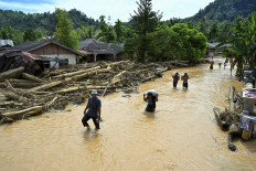 People wade through the floodwater in the aftermath of flash floods at Tukka village, Central Tapanuli, North Sumatra, on December 2, 2025. The death toll from floods and landslides that have struck Indonesia's Sumatra island since last week has risen to 712, the National Disaster Management Agency said on December 2. 