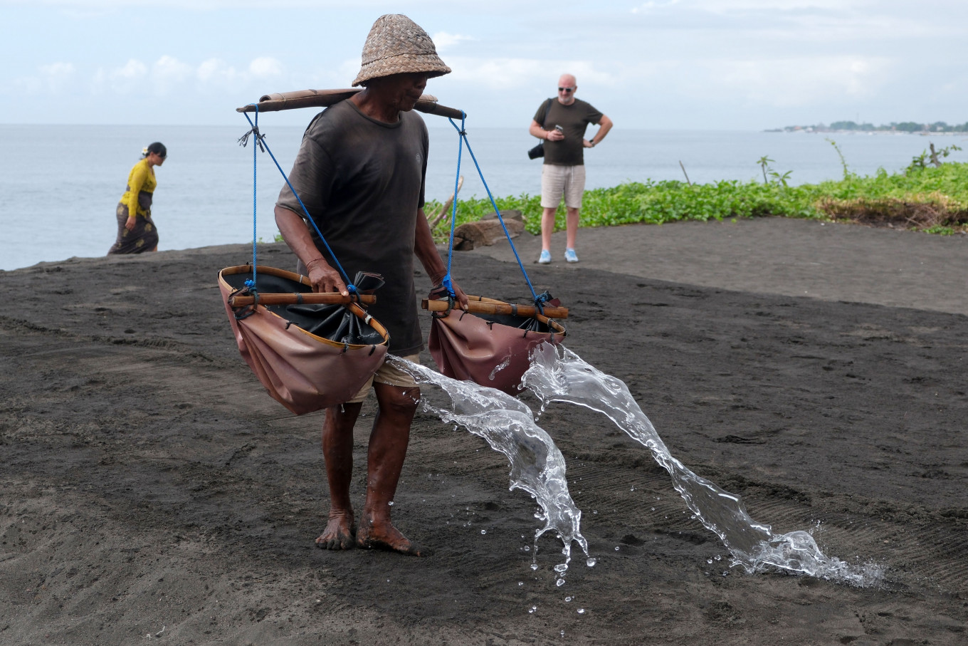 A foreign tourist watches a farmer pour seawater onto sandy fields during a traditional salt production process on Dec. 3, 2025, in Klungkung, Bali. According to local farmers, an average of 5-10 foreign tourists visit the traditional salt production site each day to observe the process and buy salt, which is sold for Rp 20,000 (US$1.20)-Rp 40,000 depending on amount.