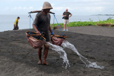 A foreign tourist watches a farmer pour seawater onto sandy fields during a traditional salt production process on Dec. 3, 2025, in Klungkung, Bali. According to local farmers, an average of 5-10 foreign tourists visit the traditional salt production site each day to observe the process and buy salt, which is sold for Rp 20,000 (US$1.20)-Rp 40,000 depending on amount.