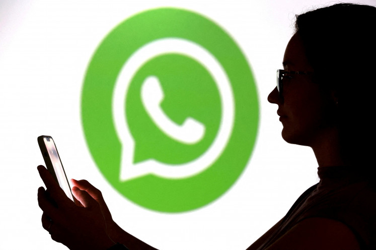 A teenager poses for a photo while holding a smartphone in front of a WhatsApp logo in this illustration photo taken Sept. 11, 2025.
