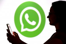 A teenager poses for a photo while holding a smartphone in front of a WhatsApp logo in this illustration photo taken Sept. 11, 2025.