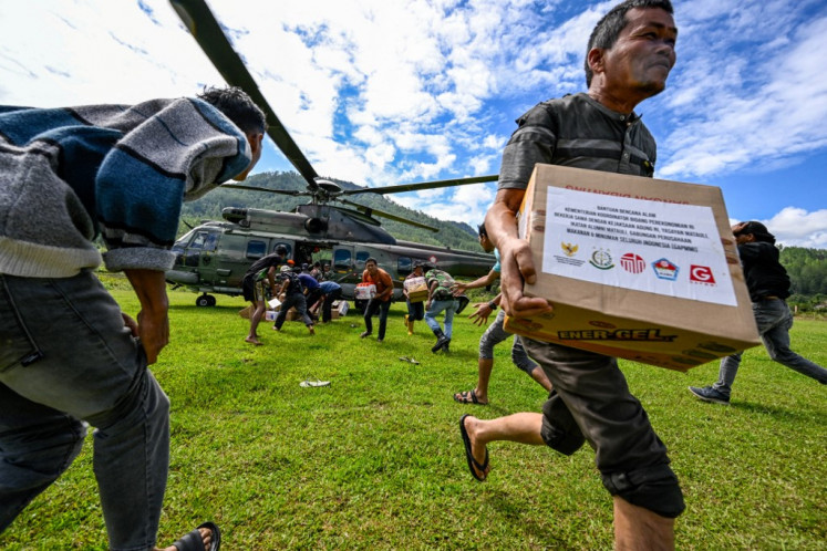 Residents carry supplies distributed by Indonesian Air Force personnel in flood affected areas in Bener Meriah district, Aceh province on December 4, 2025.