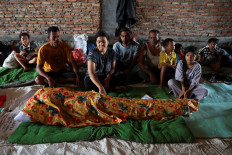 Relatives sit beside the body of Aisyah, 63, who passed away after being sick at the shelter in an area affected by a deadly flash flood following heavy rains in Kuala Simpang, Aceh Tamiang regency, Aceh, December 5, 2025. 