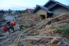 A man walks over a pile of logs and debris next to a damaged home on Dec. 5, 2025, in Geudumbak village, Langkahan district, North Aceh, after a flash flood on Nov. 26 swept them into areas along the Arakundo River Basin.