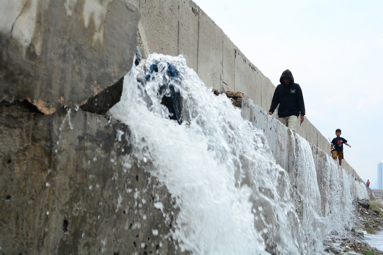 People are seen walking near a stream of water flowing from cracks in several sections of a giant seawall on Dec. 6, 2025, in a residential area in Muara Baru, North Jakarta,