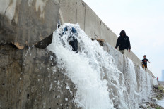 People are seen walking near a stream of water flowing from cracks in several sections of a giant seawall on Dec. 6, 2025, in a residential area in Muara Baru, North Jakarta,