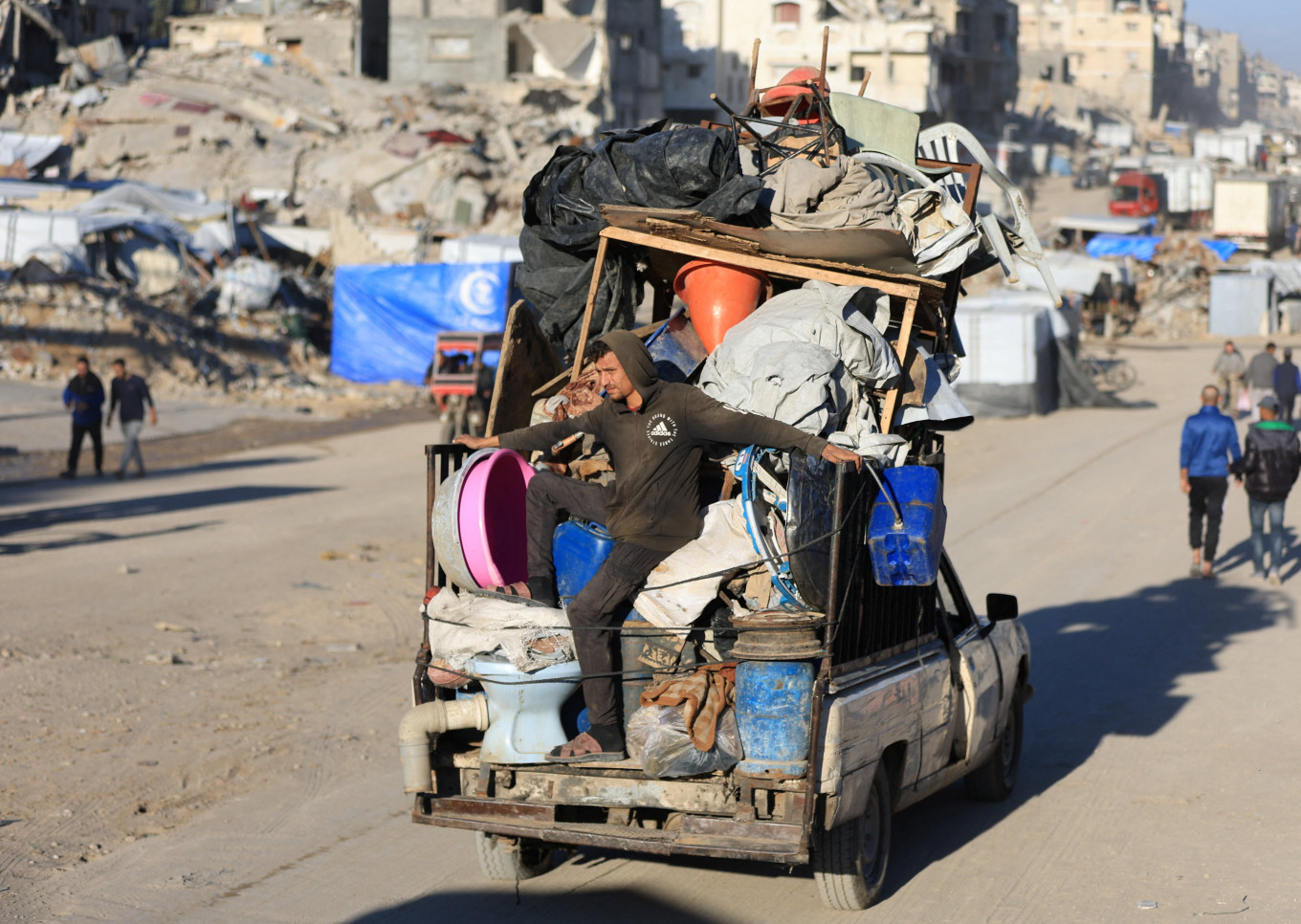 A man travels on a pickup truck loaded with belongings and driving past damaged buildings in Gaza City on December 2, 2025.